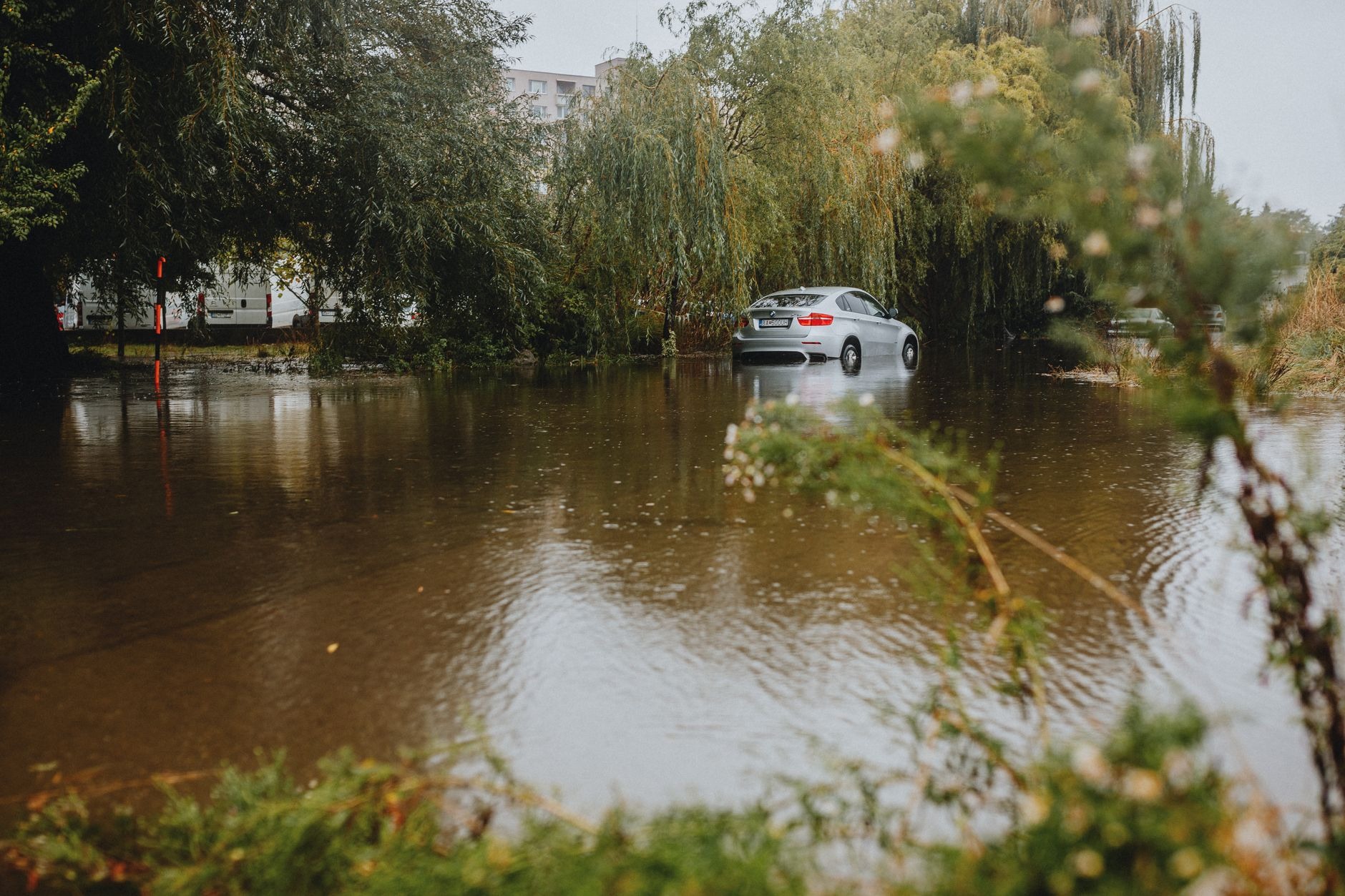 Ein Kombi steht bei Nacht auf einer überfluteten Berliner Straße, die Türschwellen zur Hälfte im Wasser, Regen fällt in